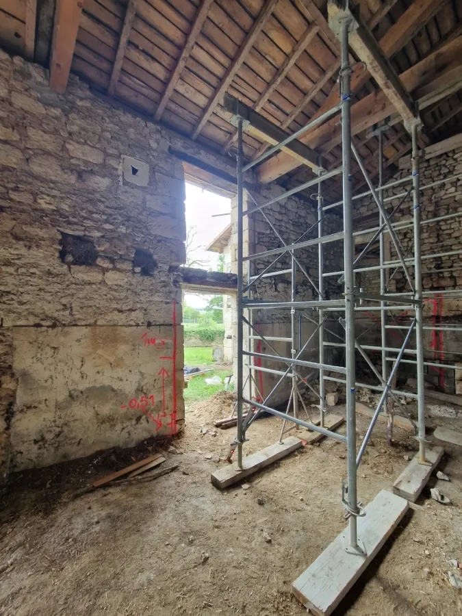 Création d'une ouverture dans un mur en pierre lors de la rénovation d'une grange, avec échafaudage