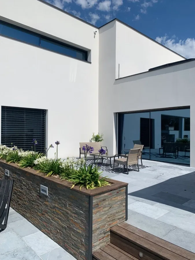 Façade blanche d’une maison contemporaine avec baie vitrée coulissante et terrasse en dalles