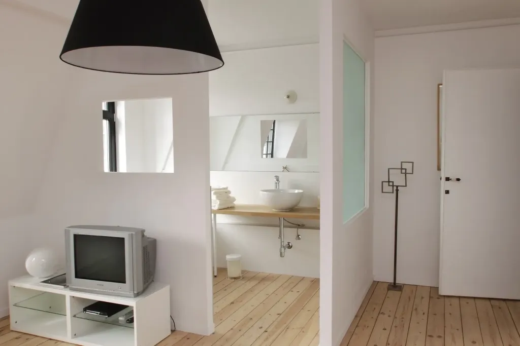 Intérieur lumineux aux murs blancs avec cloisons séparant un coin salon d'une salle d'eau, parquet clair au sol