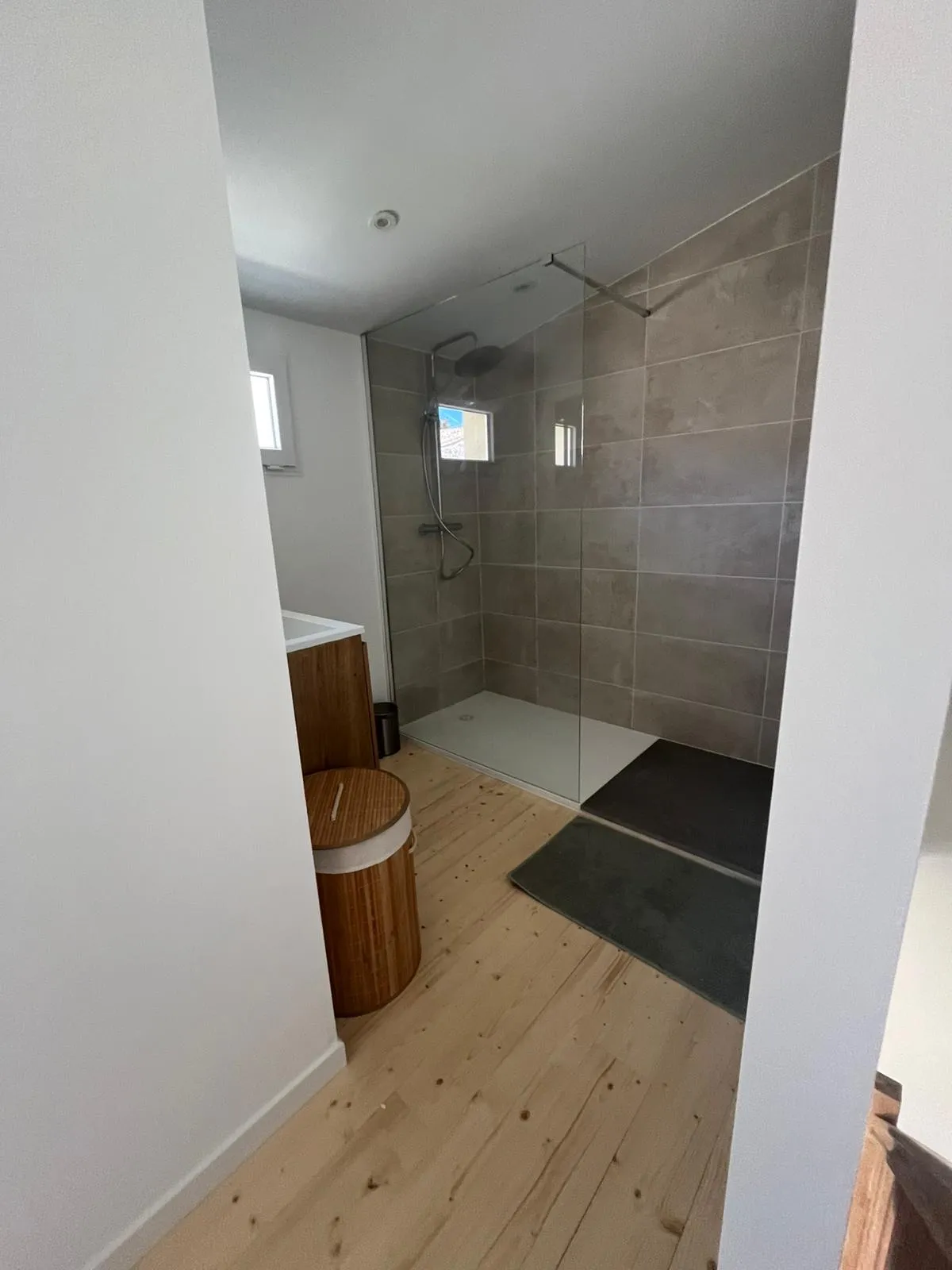 Douche à l'italienne aux murs carrelés taupe, avec pommeau de pluie et paroi en verre