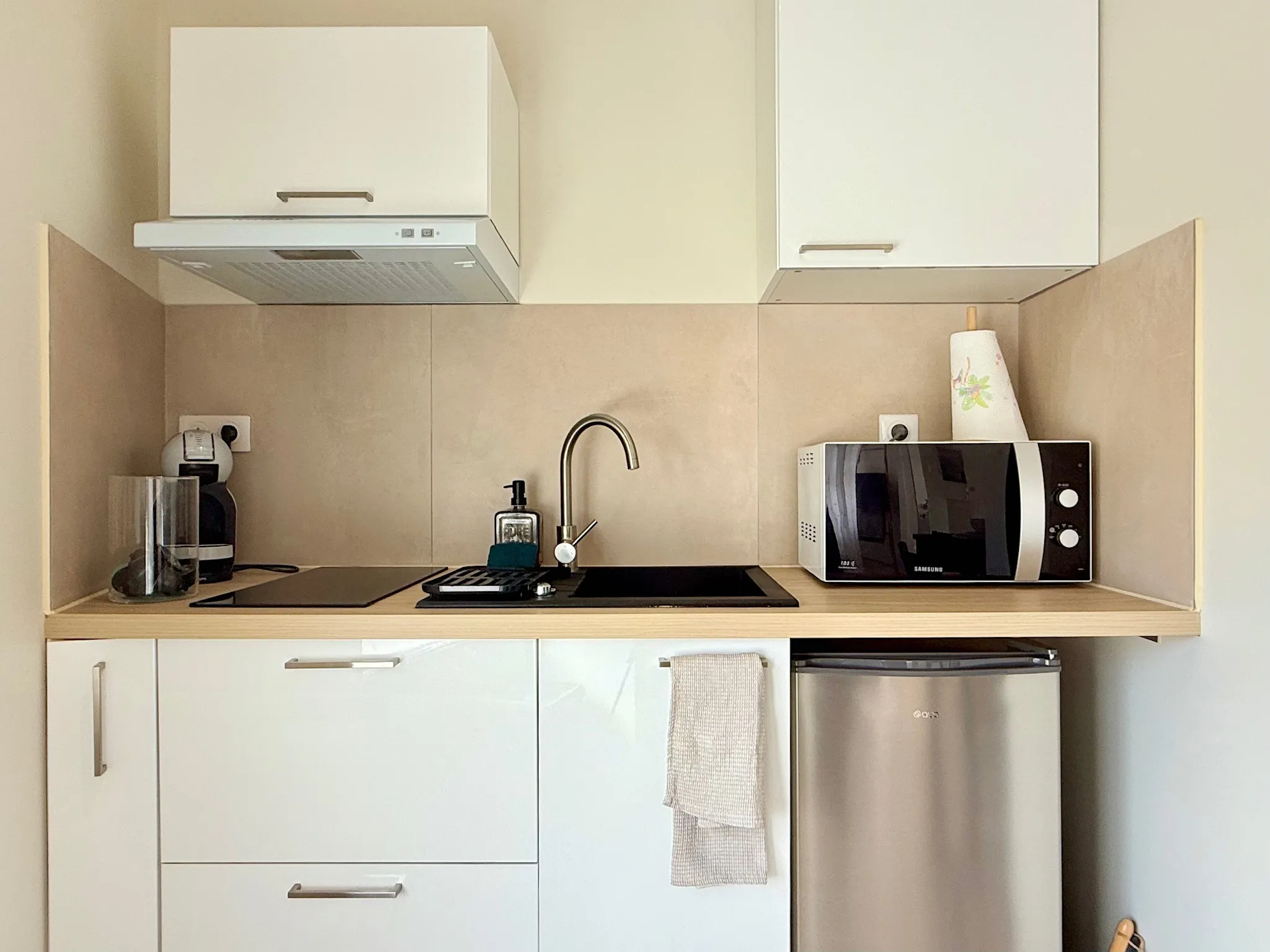 Kitchenette avec crédence en grands carreaux beiges derrière l'évier et la plaque de cuisson