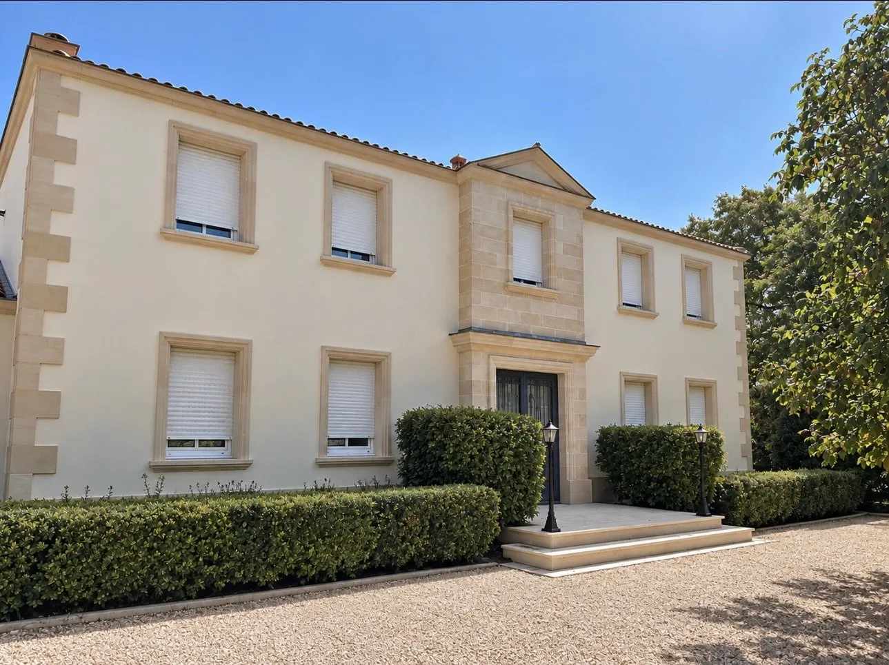 Maison à étage à façade enduite claire, encadrements et fronton en pierre autour de l'entrée