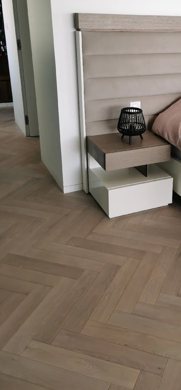 Parquet en chêne clair posé en point de Hongrie dans une chambre, près d'une table de chevet