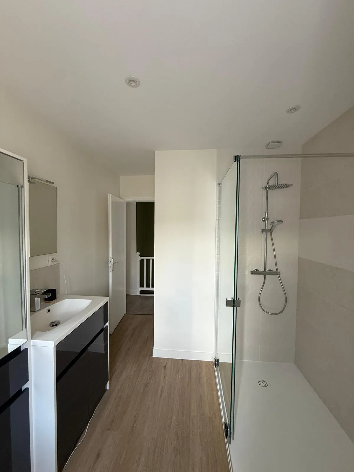 Salle de bain avec meuble vasque blanc et noir, miroir et douche vitrée avec robinet thermostatique