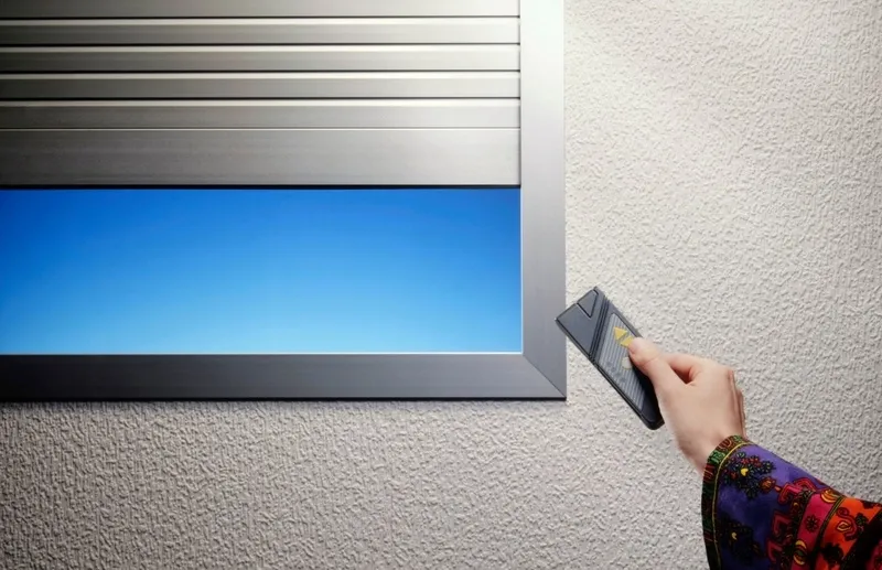 Volet roulant en aluminium à demi ouvert sur une fenêtre, commandé par une télécommande